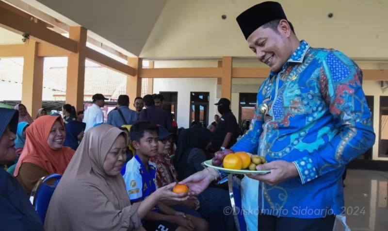 Plt Bupati Sidoarjo Subandi berikan buah kepada warga yang sedang mengambil bantuan beras CPP di Kedungsukodani, Kecamatan Balongbendo. 